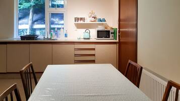 A kitchen with a window, microwave, kettle, and a table with chairs.