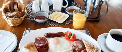 Ein Frühstückstisch mit Eiern, Würstchen und Toast, sowie Beilagen, einer Kaffeetasse und einem Glas Fruchtsaft.
