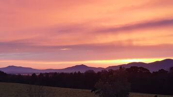 A sunset over a mountainous landscape with silhouettes of trees and a field.
