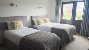A hotel room with two beds, a window with curtains, and a view of the outdoors.
