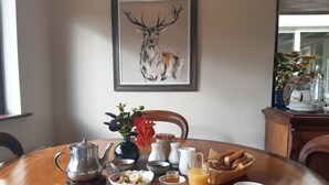 A breakfast table with a variety of food items, a coffee cup, and a framed deer painting on the wall.