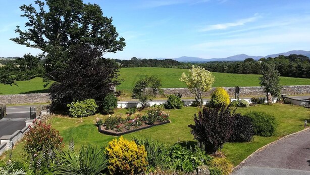 A well-maintained garden with a variety of plants and trees, a stone wall, and a clear view of the countryside and mountains in the distance.
