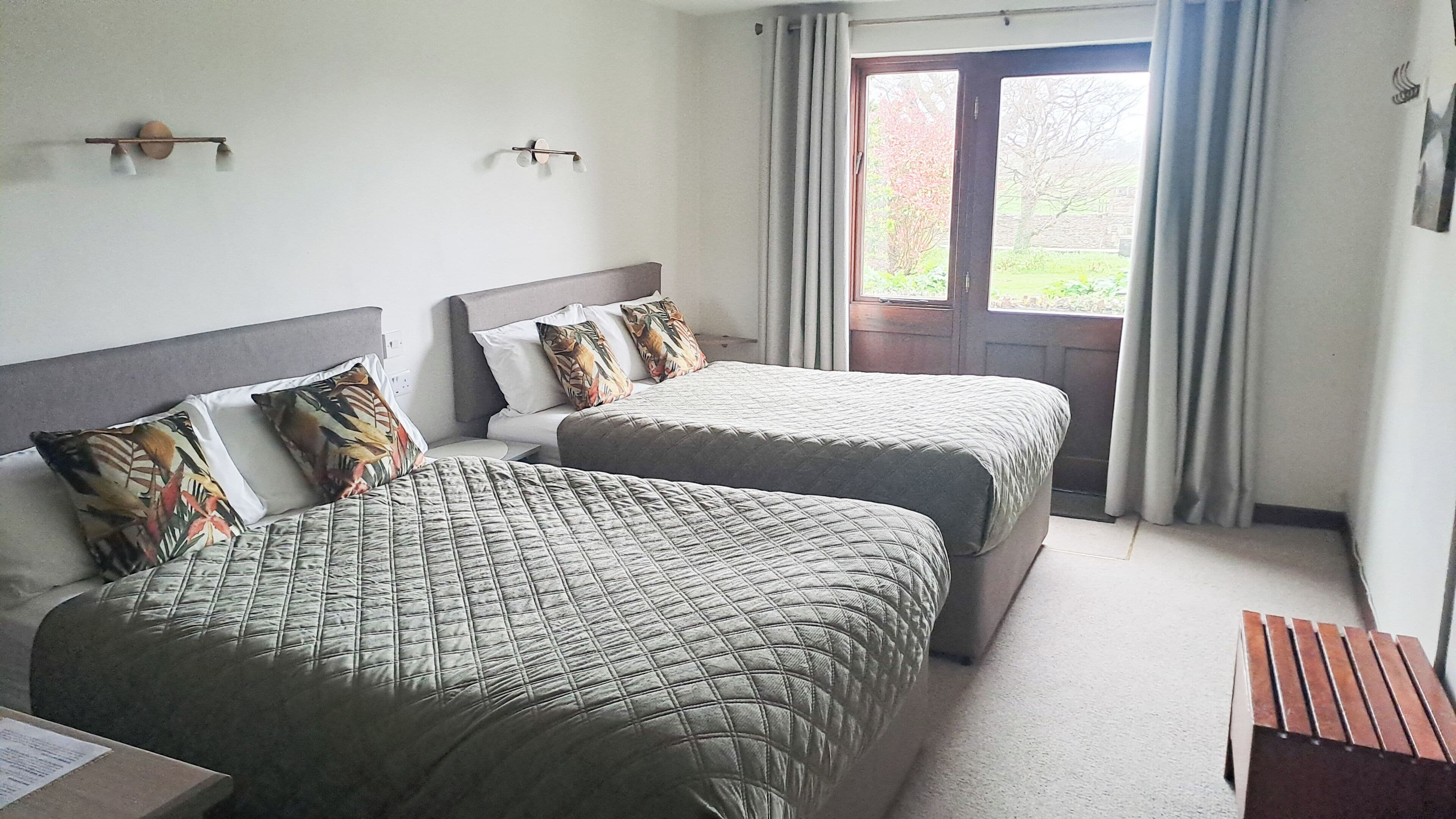 A double room with two beds, a wooden bench, a window with curtains, and a door.