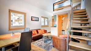 A modern living room with a sofa, a dining table, and a staircase. - Chalet Abacus (Zermatt)
