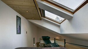 A high-ceilinged room with a skylight, a bed, a green chair, and a framed picture on the wall. - Chalet Abacus (Zermatt)