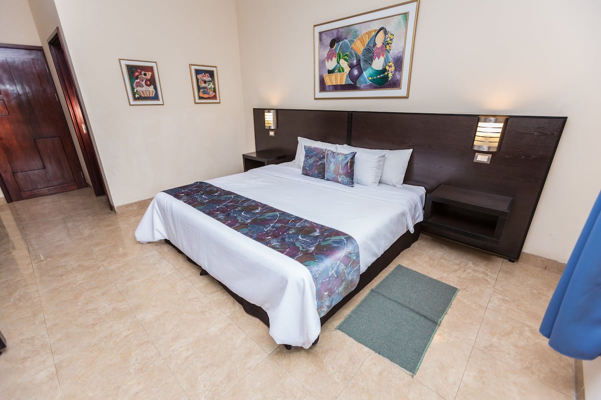 A hotel room with a large bed, a nightstand, a wall-mounted lamp, and artwork on the wall.