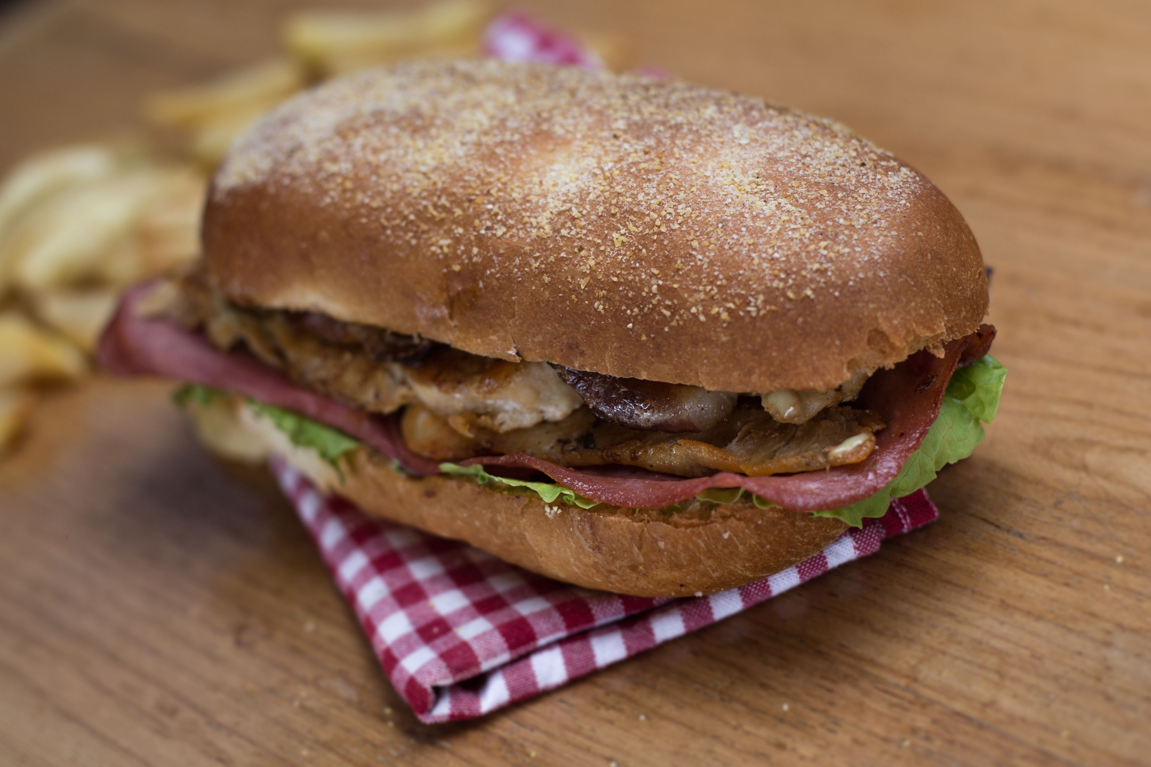Un sandwich posé sur une table en bois, avec une serviette à carreaux rouges et blancs placée en dessous.