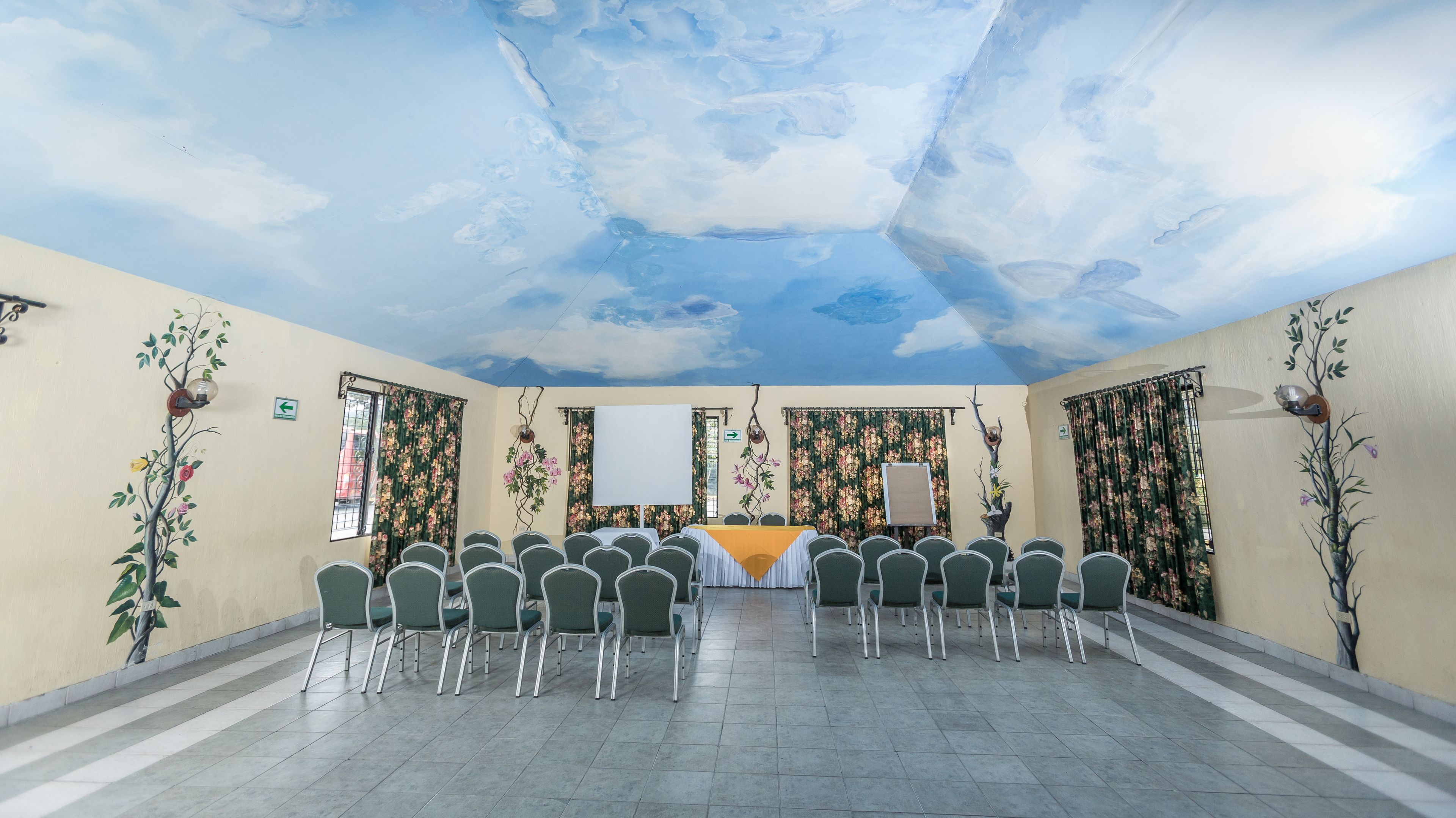 A conference room with a long table, chairs, floral wall decorations, and a ceiling mural.