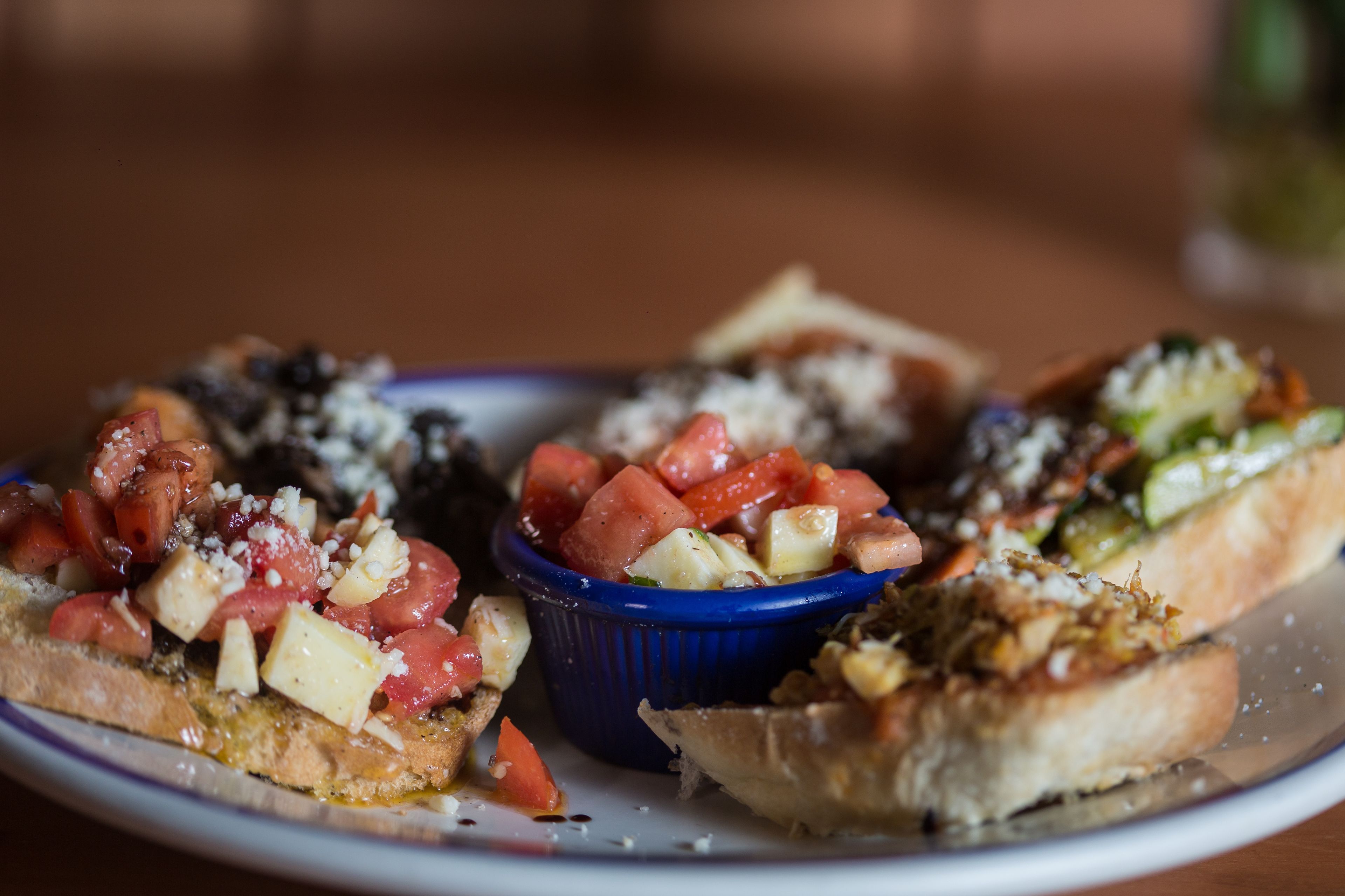 Un plato con diversos alimentos, incluyendo un cuenco azul que contiene tomates y queso en cubos.