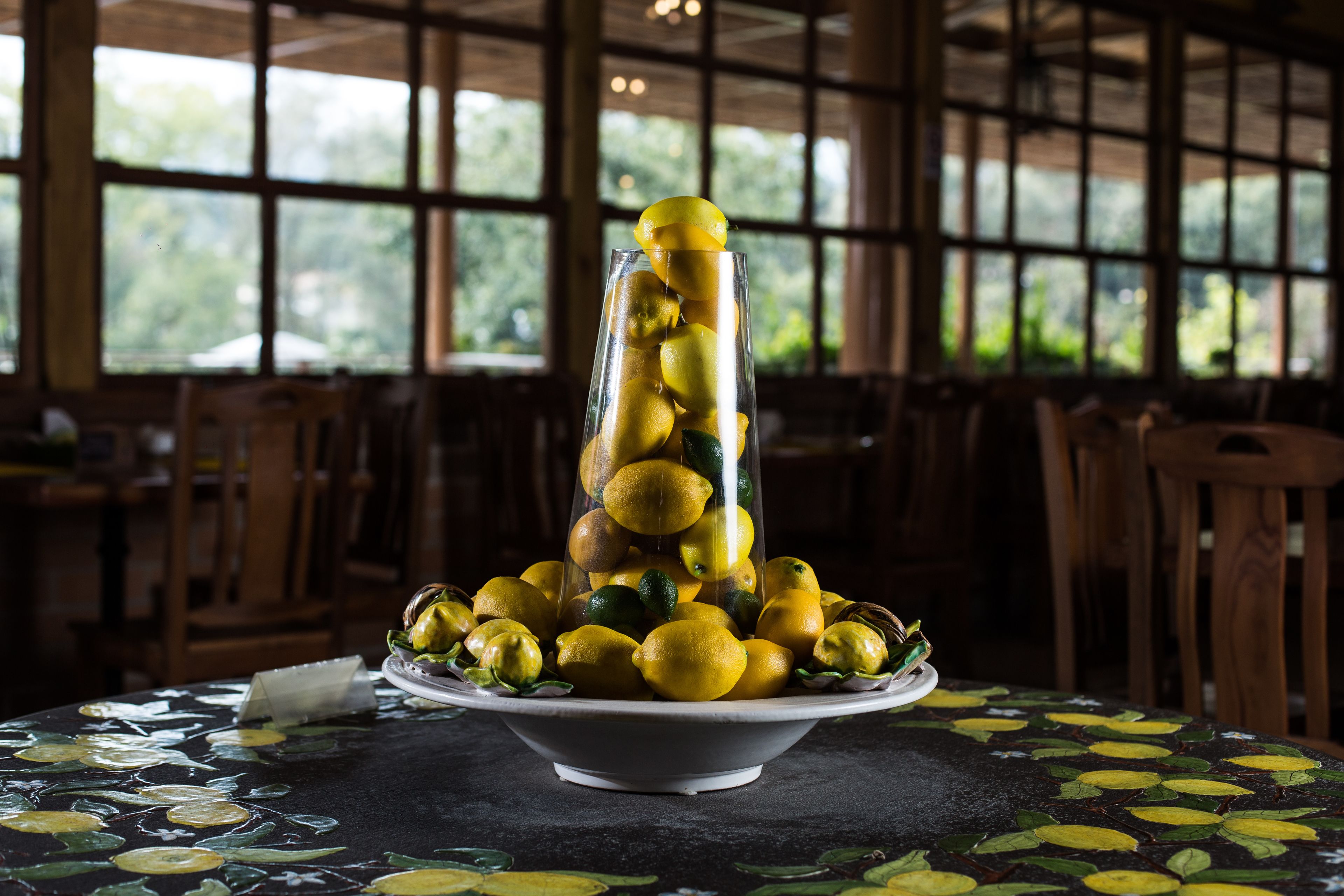 Una mesa con un centro de mesa de vidrio decorativo que contiene limones y limas, sobre un mantel con estampado de limones.