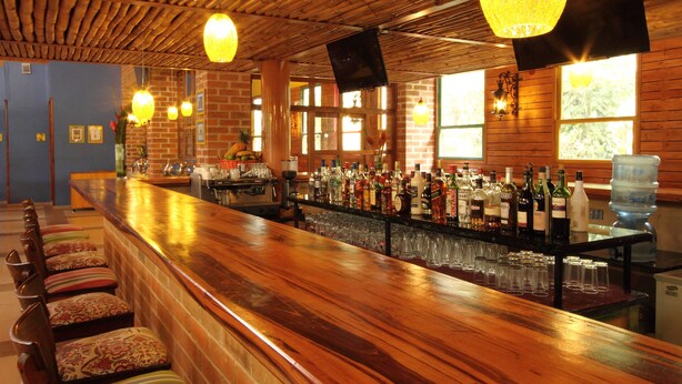 Zona de bar con una barra de madera larga, varios taburetes y una variedad de botellas y vasos.