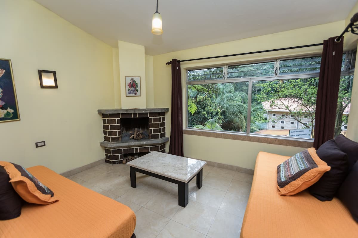A living room with a fireplace, a sofa, a coffee table, and a large window with curtains.