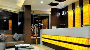 Een moderne receptie met een bank, een glazen salontafel en een receptiebalie met een warm verlicht paneel.