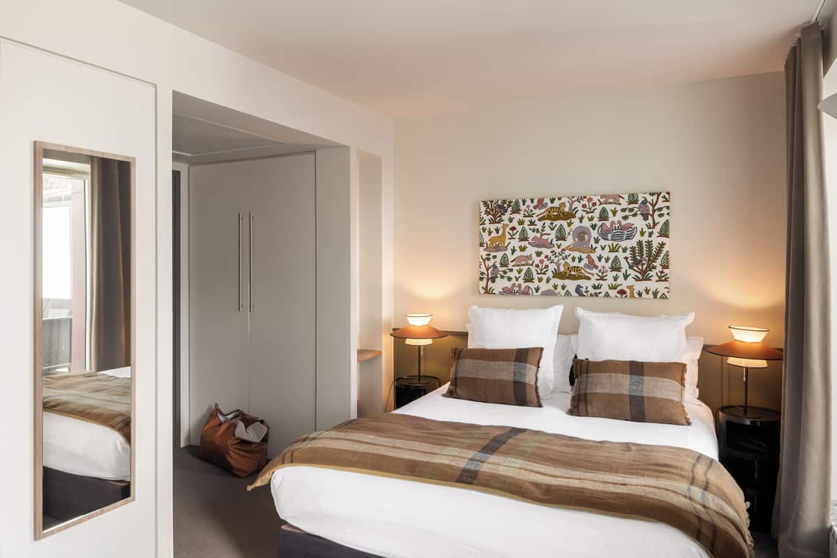 Ein Hotelzimmer mit Bett, Nachttischlampen, einem Spiegel, einem Kleiderschrank und einer Wand mit dekorativem Muster.