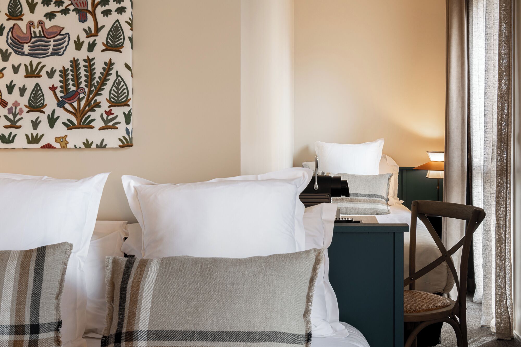 A hotel room with two beds, a desk, a chair, and a wall with a nature-themed painting.