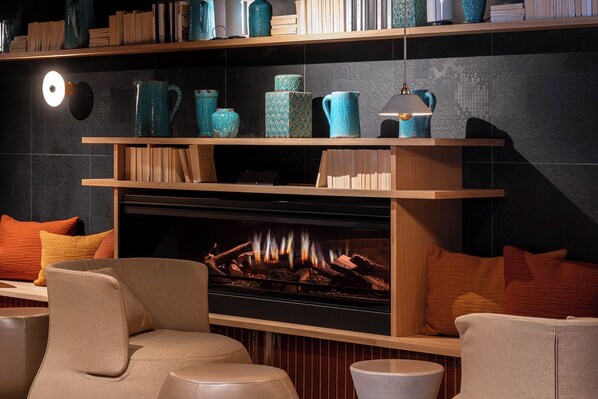 A cozy seating area with a fireplace, shelves with decorative items, and books. - Hôtel L'Adresse (Saint-Malo)