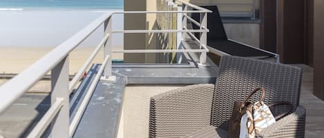 A balcony with wicker furniture and a bag, overlooking a beach.