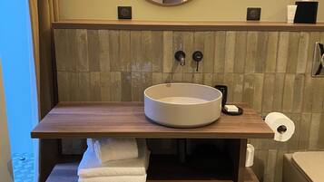 A bathroom with a round sink, wooden vanity, and a mirror with wall sconces.