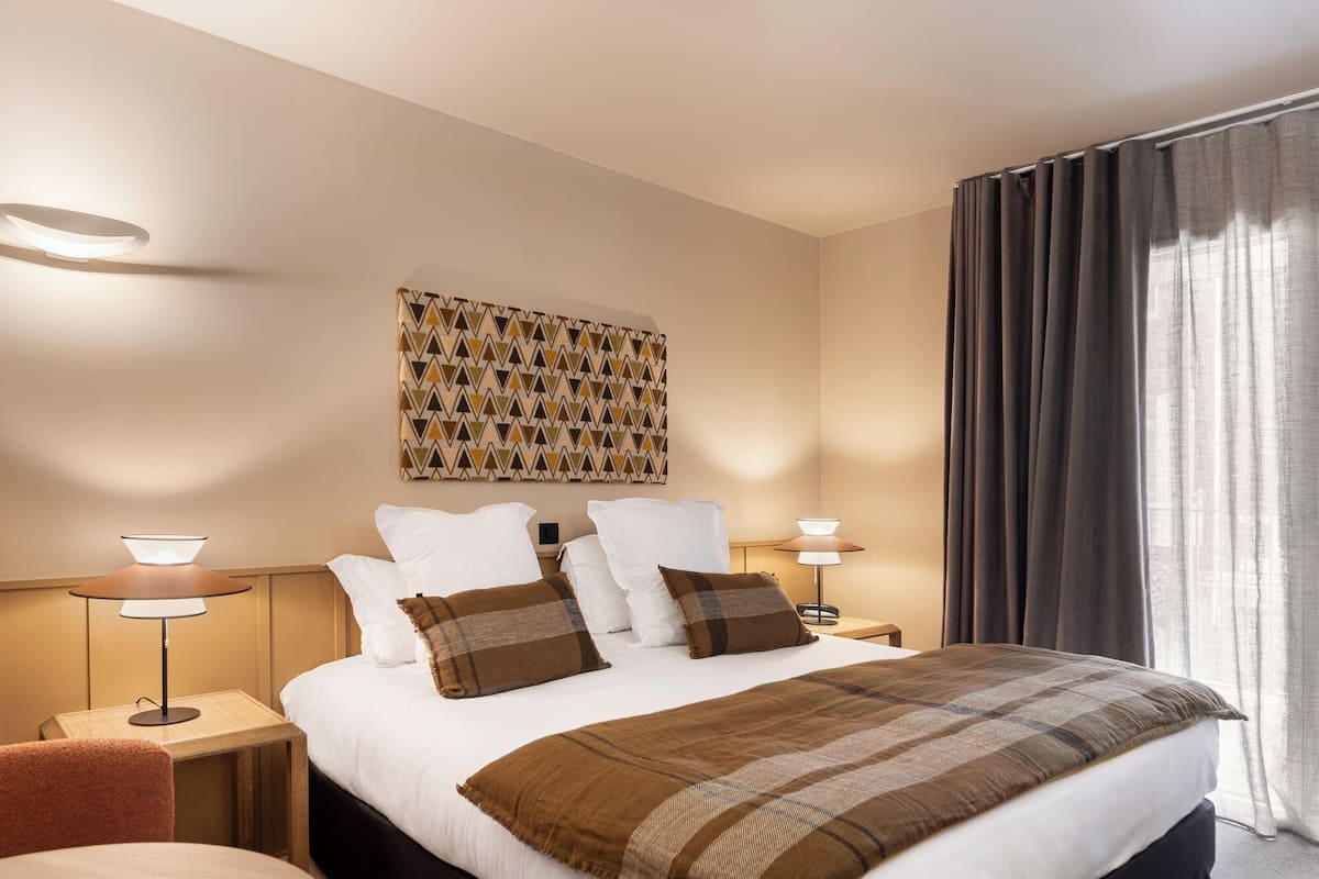 Ein Hotelzimmer mit einem großen Bett, zwei Nachttischen mit Lampen, einem Wandbild und einem Fenster mit Vorhängen.