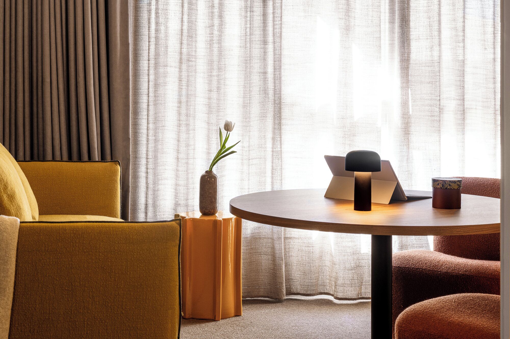 A modern room with a round wooden table, a laptop, a vase with a plant, and a coffee cup.