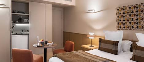 Una habitación de hotel con una cama, una mesita con alimentos para el desayuno, una silla, una lámpara y un estante en la pared.