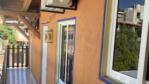 Un pasillo con suelo de baldosas, una ventana con marco azul y un equipo de aire acondicionado instalado en la pared.