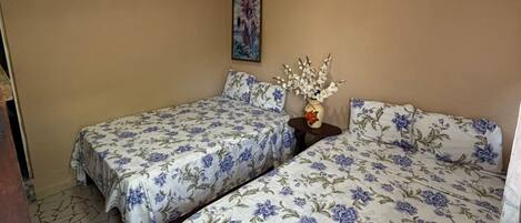A bedroom with two beds, a small table with a vase, and a painting on the wall.