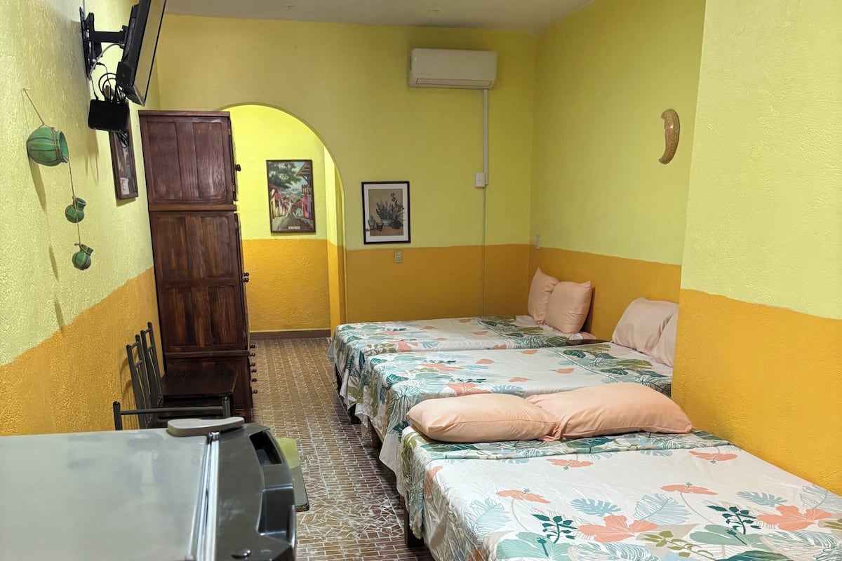A room with two beds, a wooden wardrobe, a television mounted on the wall, and a tiled floor.