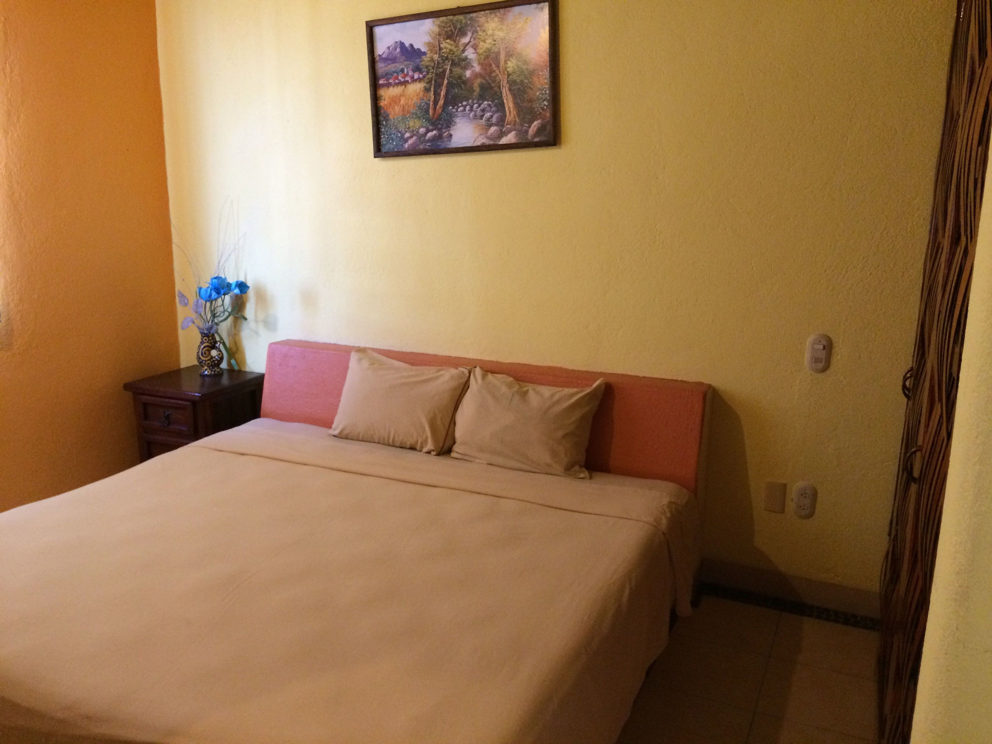 A bedroom with a bed, a nightstand with a vase of flowers, and a painting on the wall.