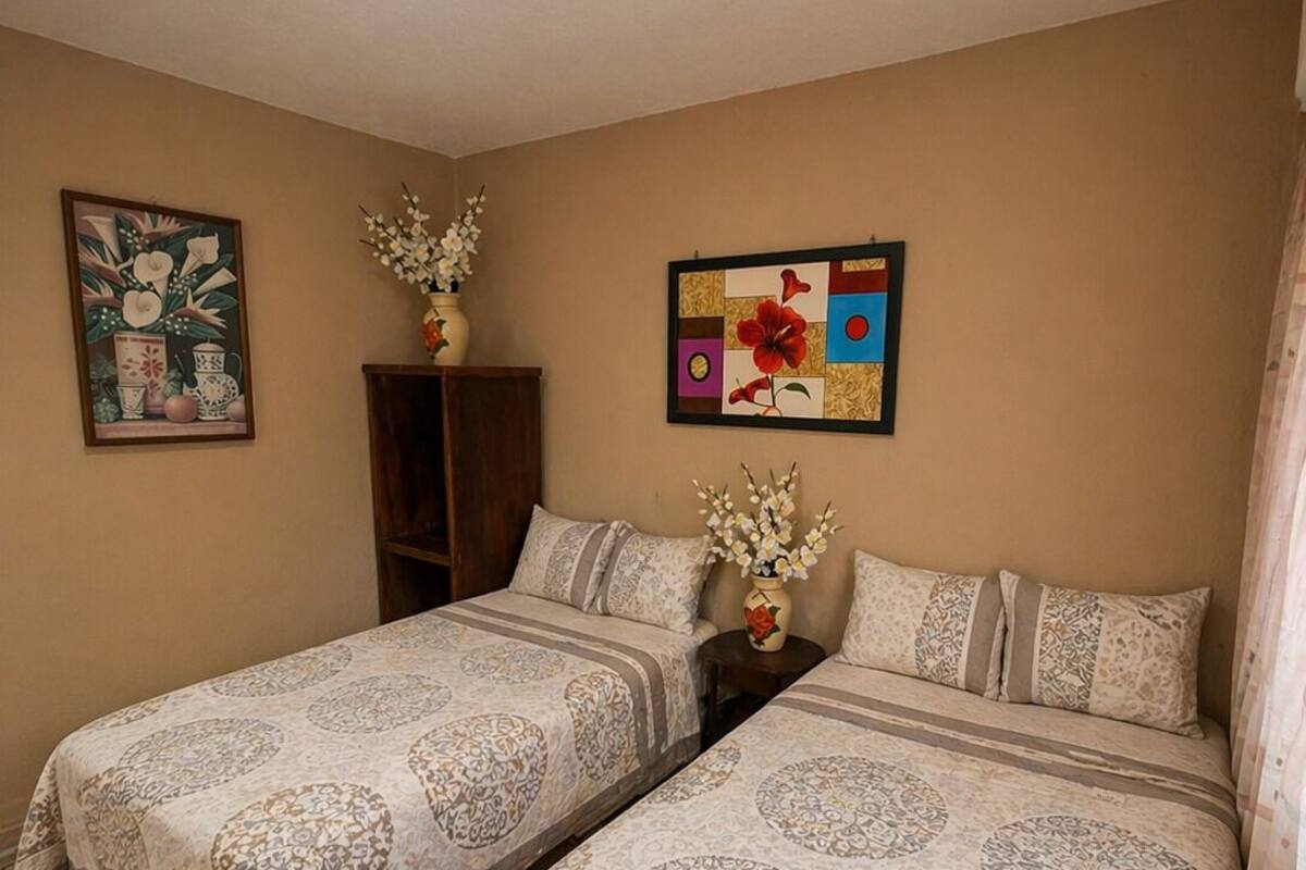 A room with two beds, a ceiling light, a cabinet, and two wall decorations.