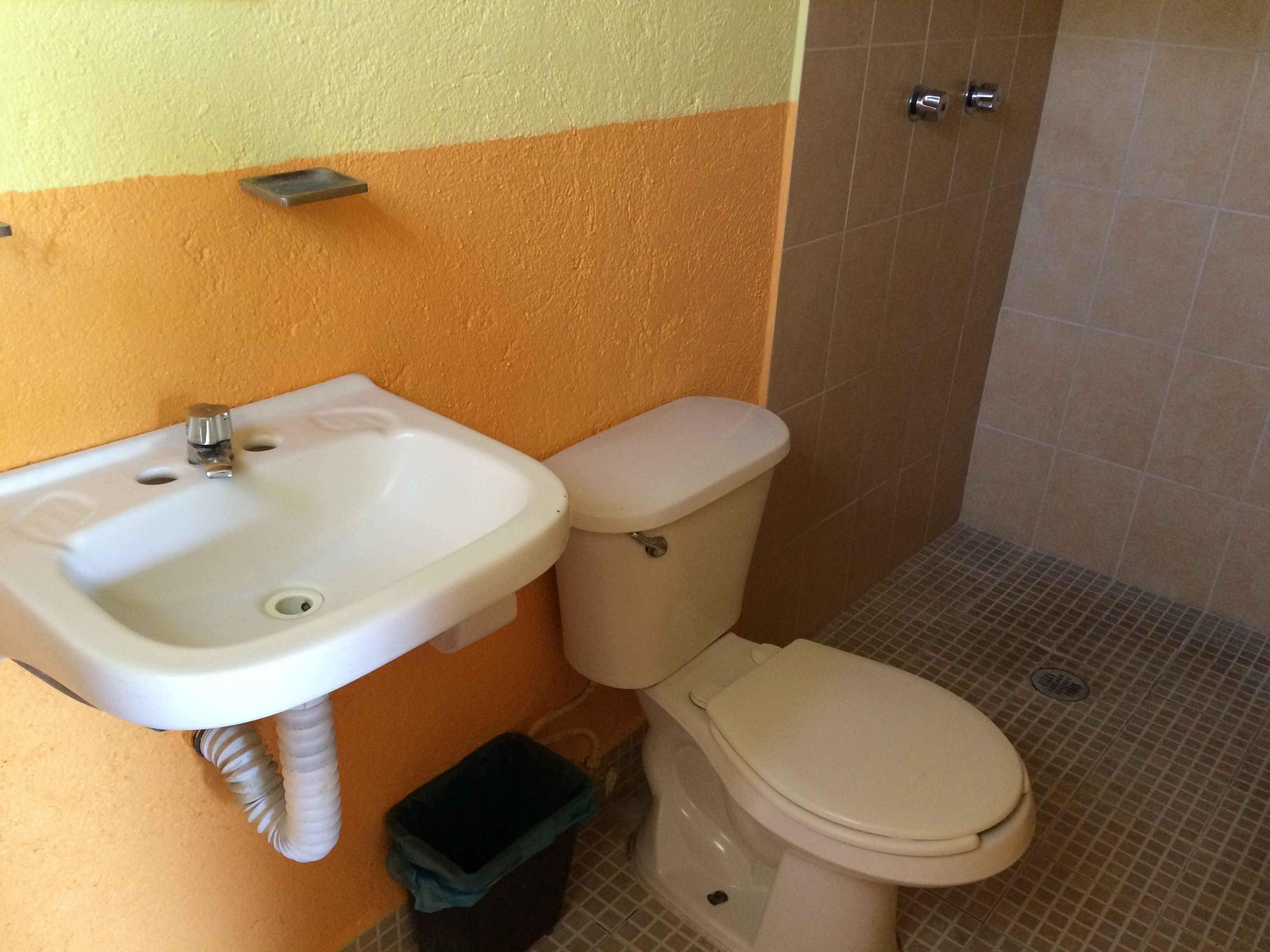 Baño con lavamanos blanco, inodoro y cubo de basura.
