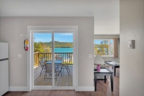 A room with a sliding glass door leading to a balcony with a view of a lake and hills. - Bayside Inn & Marina (Cooperstown)