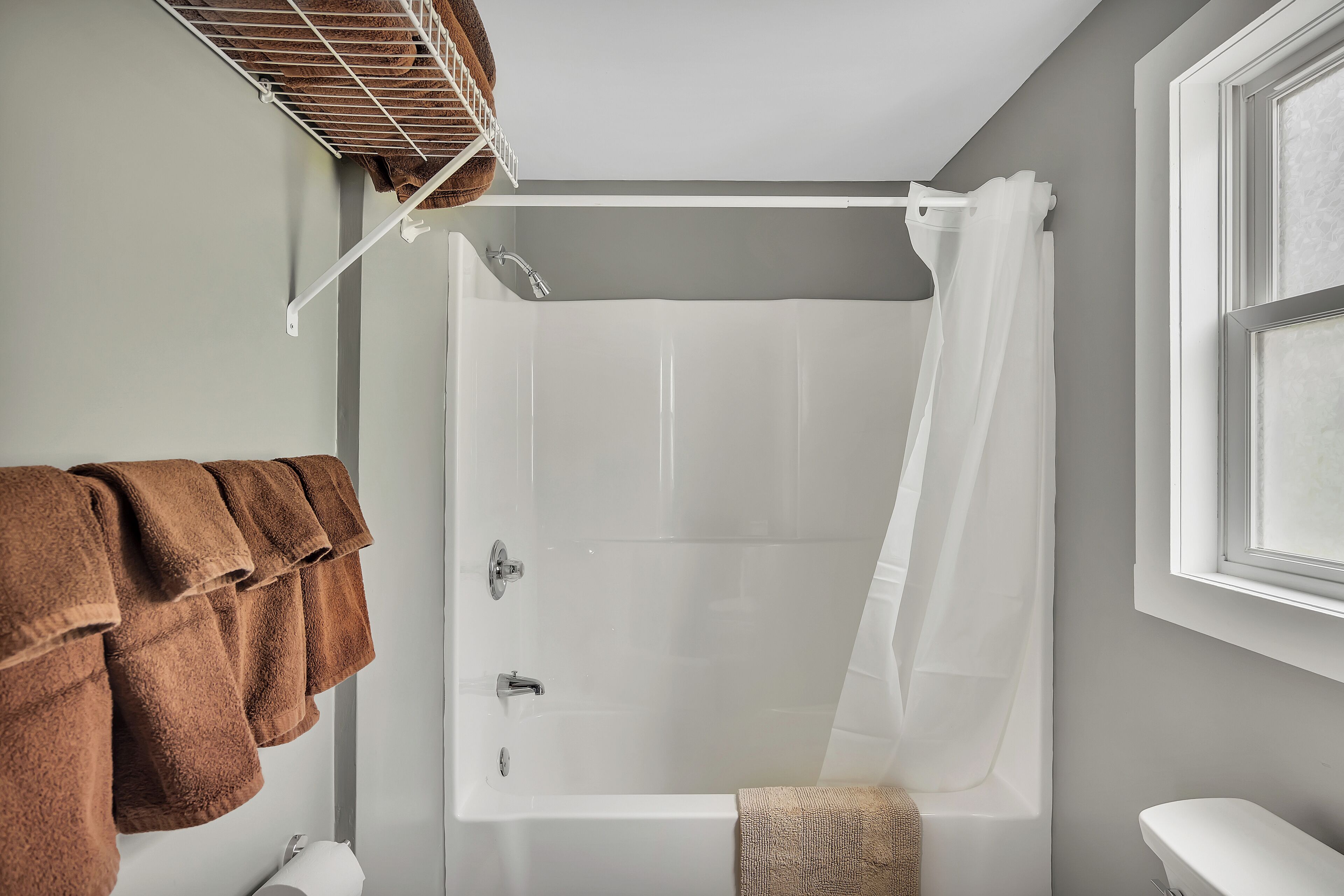 A bathroom with a bathtub, a towel rack with brown towels, and a window.