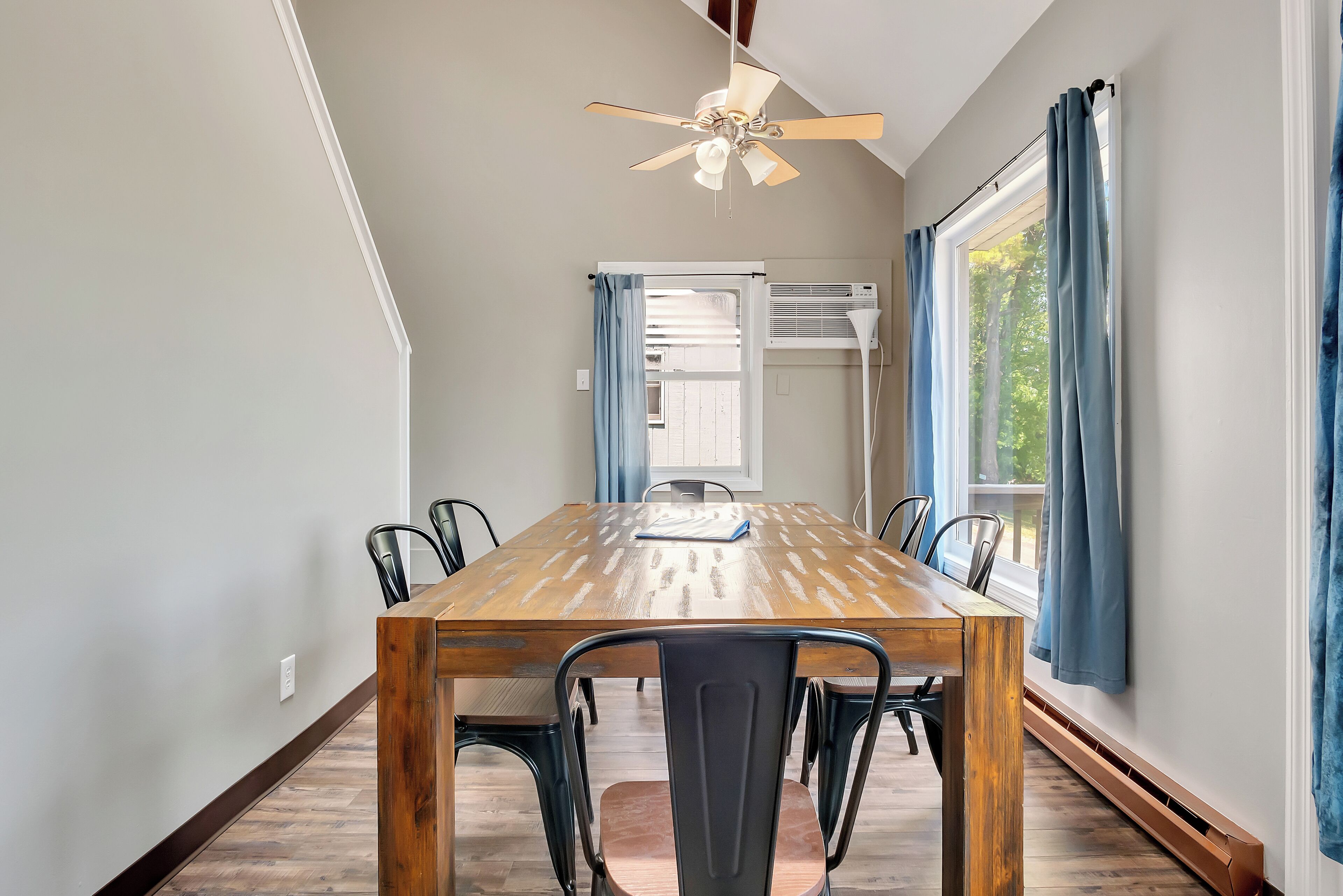 A dining area with a wooden table, black chairs, a ceiling fan, and a window with curtains.