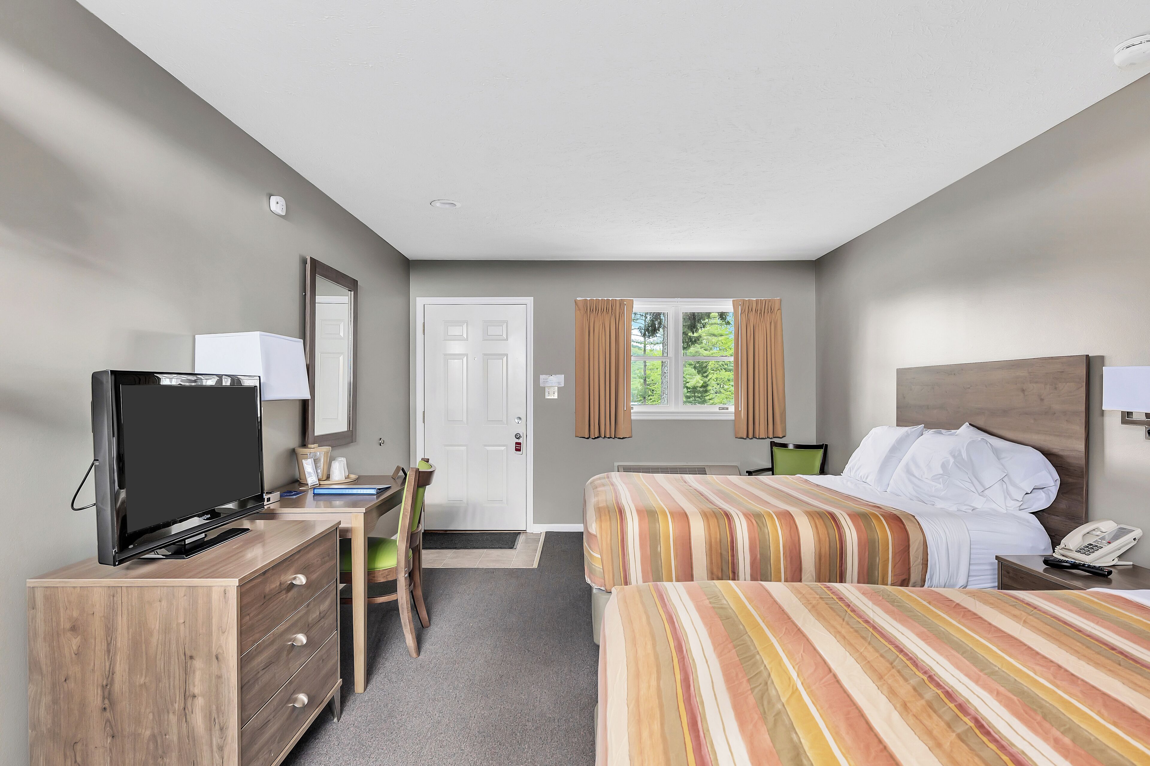 A hotel room with two beds, a desk with a chair, a television, and a window with curtains.