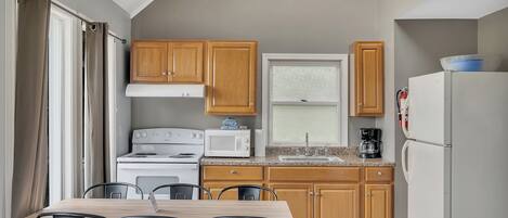 A compact kitchen with wooden cabinets, a white stove, a microwave, and a refrigerator.