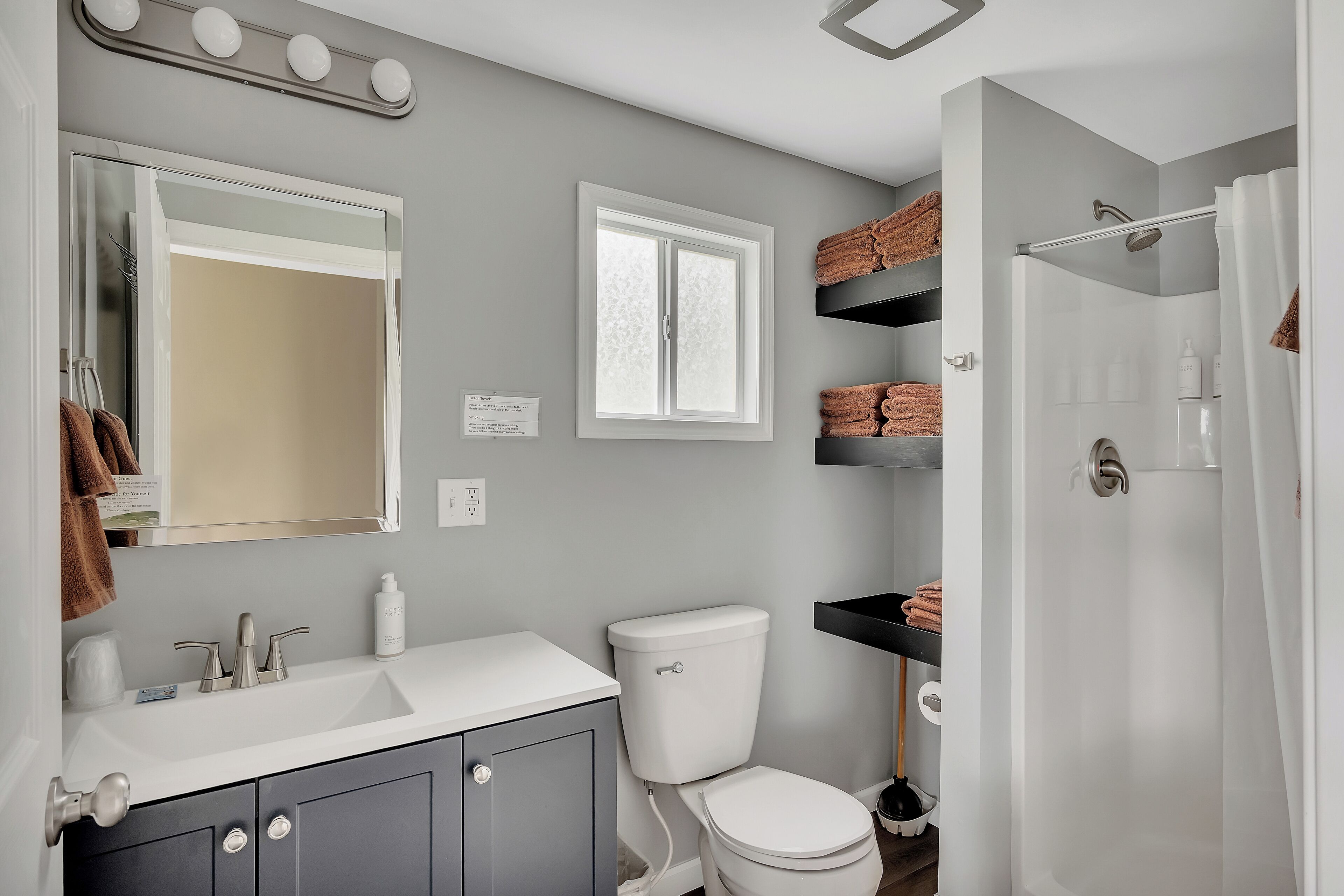 A bathroom with a white sink, a toilet, a shower, and shelves with towels.