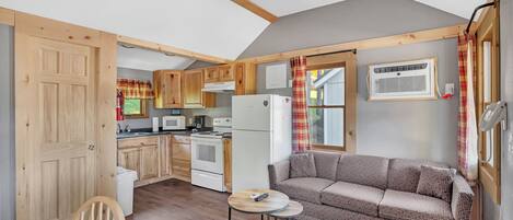 A compact kitchen with wooden cabinets, a dining area with a round table and chairs, and a sofa.