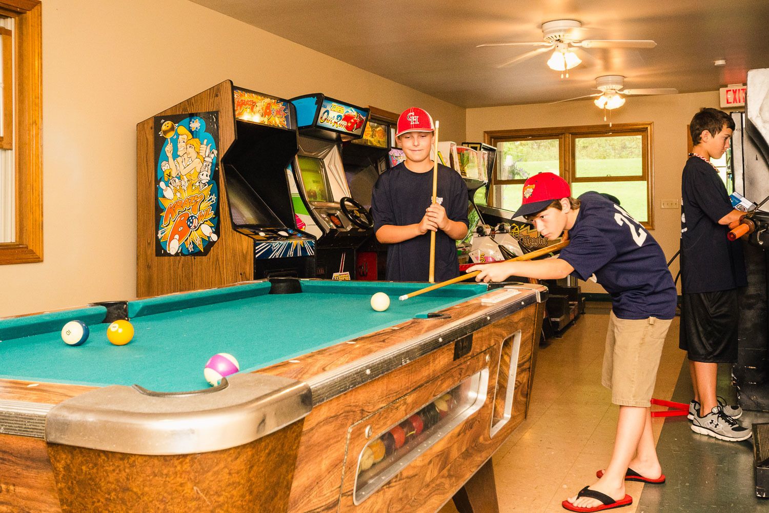 A pool table in a room with arcade games and a ceiling fan.