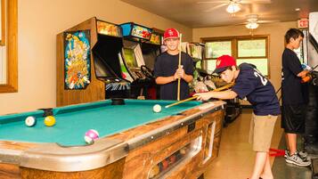 A pool table in a room with arcade games and a ceiling fan.
