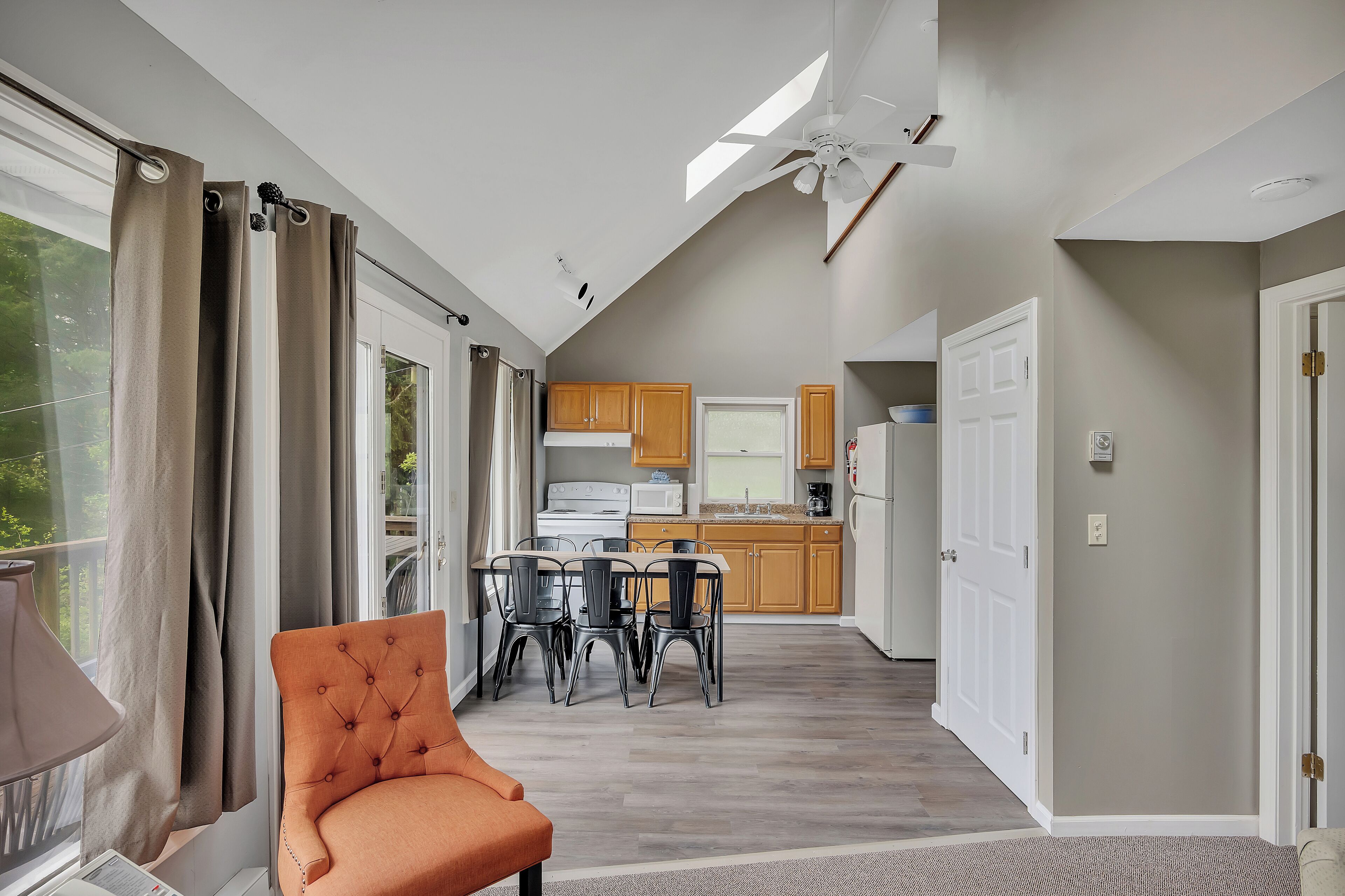 A modern kitchen with wooden cabinets, a dining area with a table and chairs, and a ceiling fan.