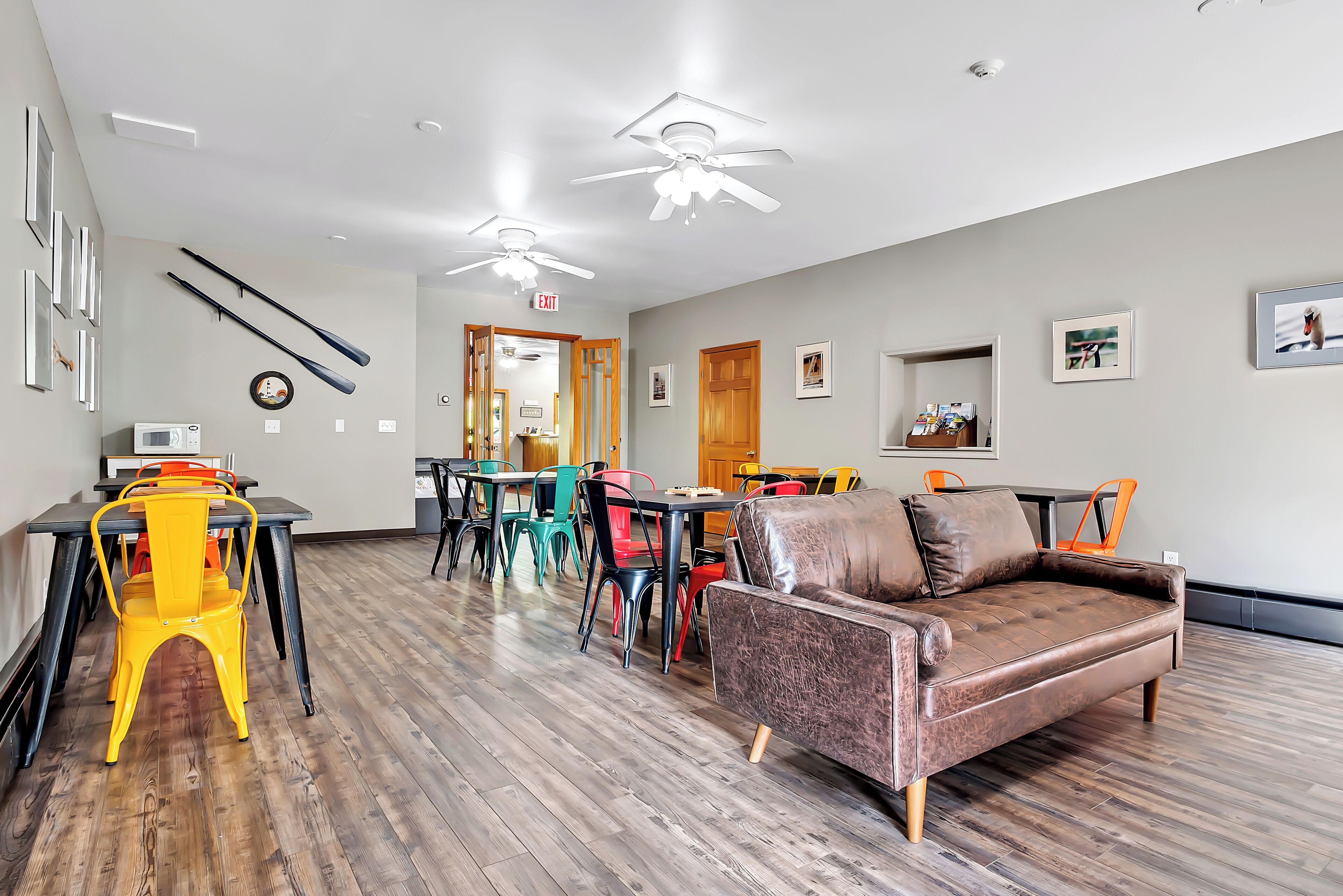 A spacious room with a brown leather sofa, colorful chairs, a dining table, and a ceiling fan.