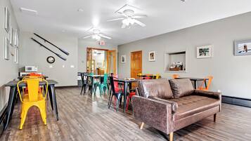A spacious room with a brown leather sofa, colorful chairs, a dining table, and a ceiling fan.