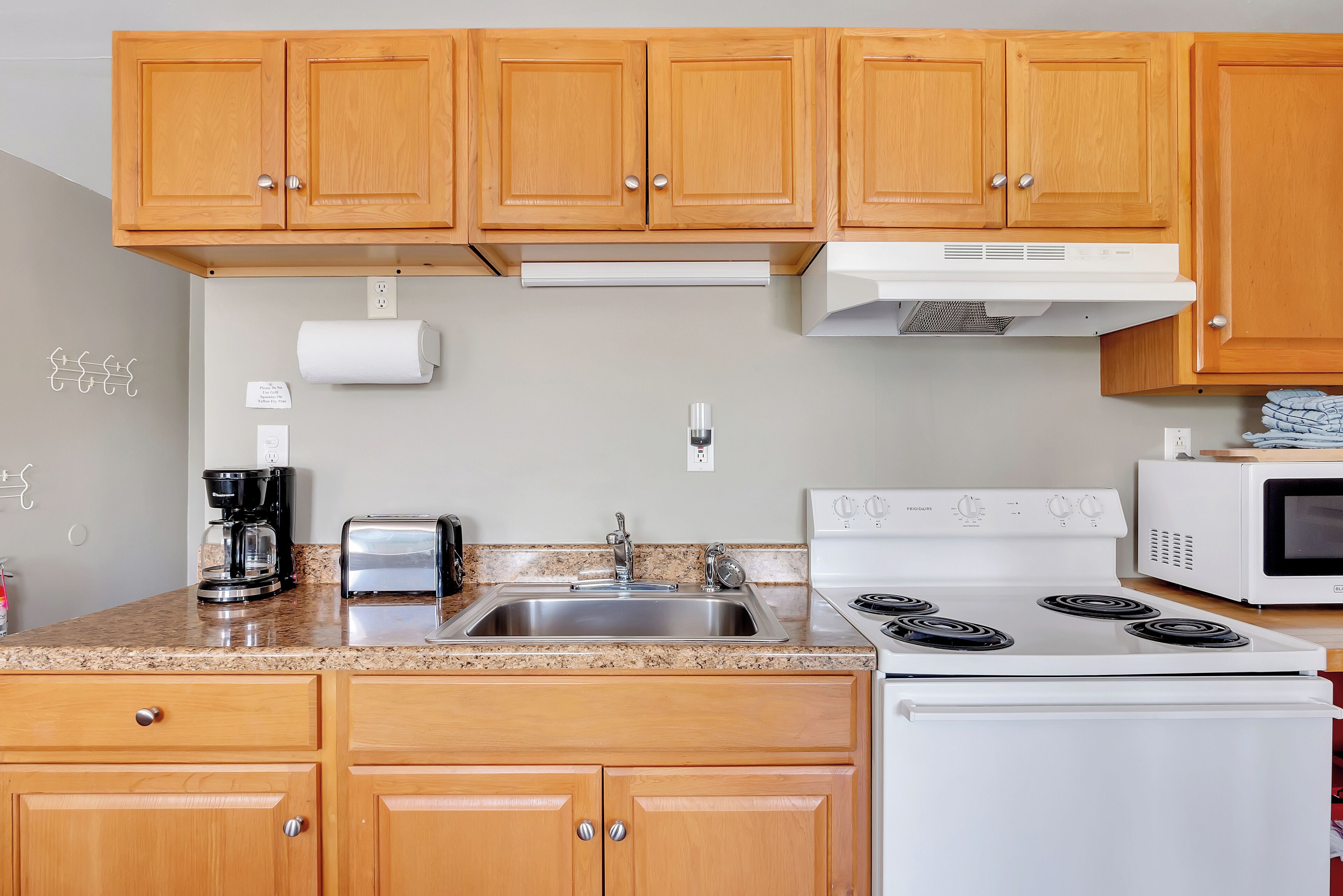 A kitchen with wooden cabinets, a stainless steel sink, a white stove, and a microwave.