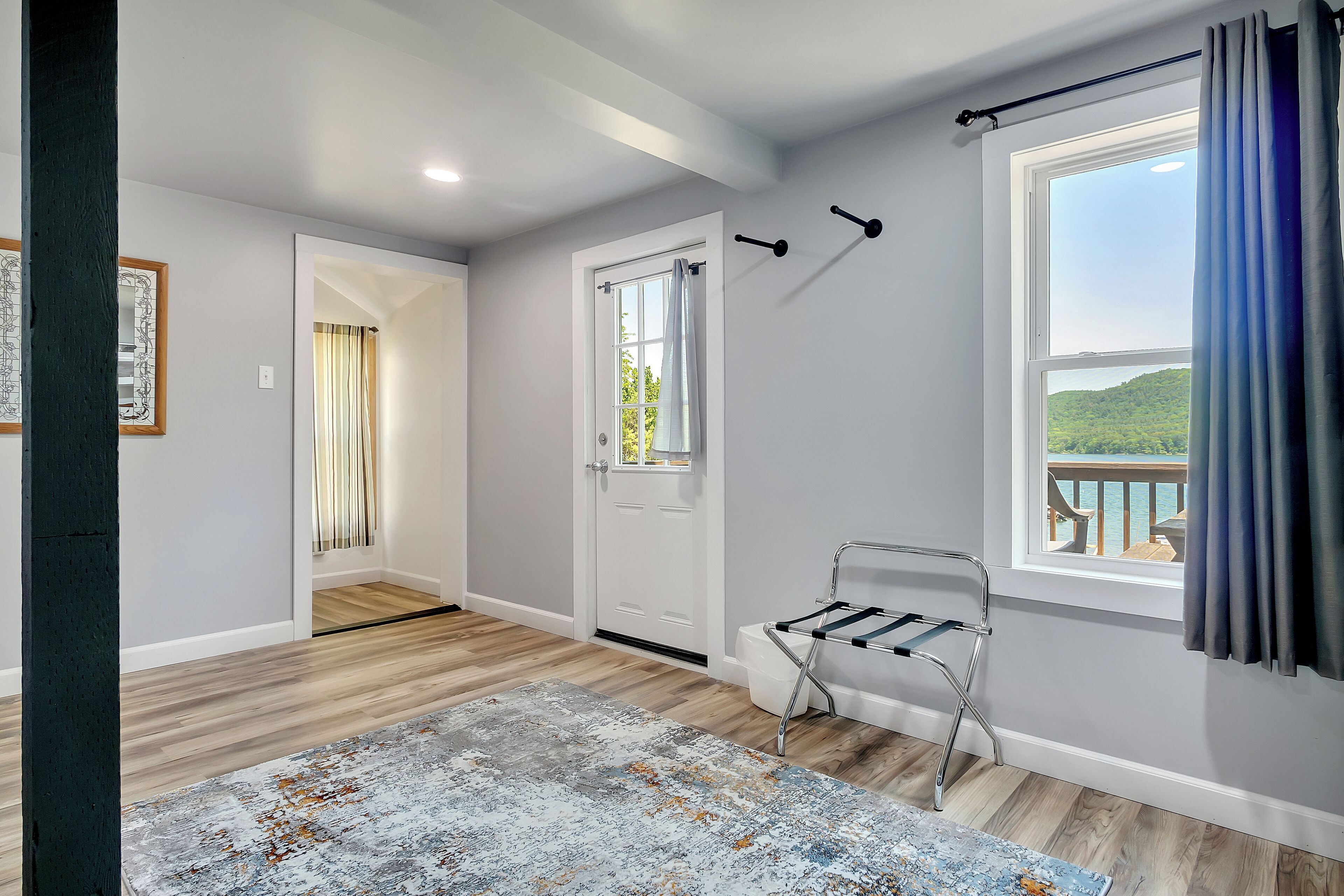 A room with a wooden floor, a door leading to another room, a window with a view of a deck, and a metal chair.