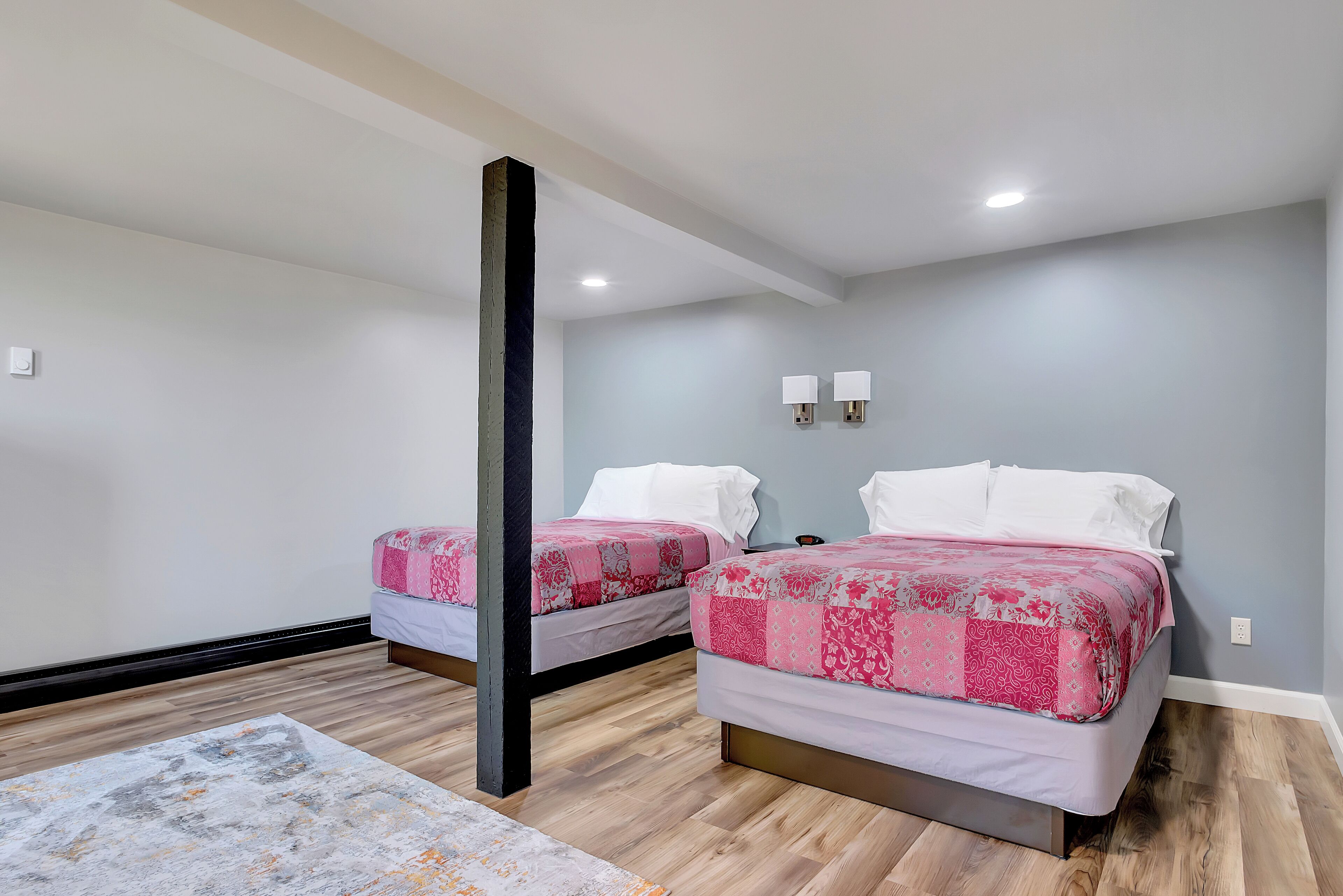Quarto com duas camas, piso de madeira, parede cinza e teto branco.
