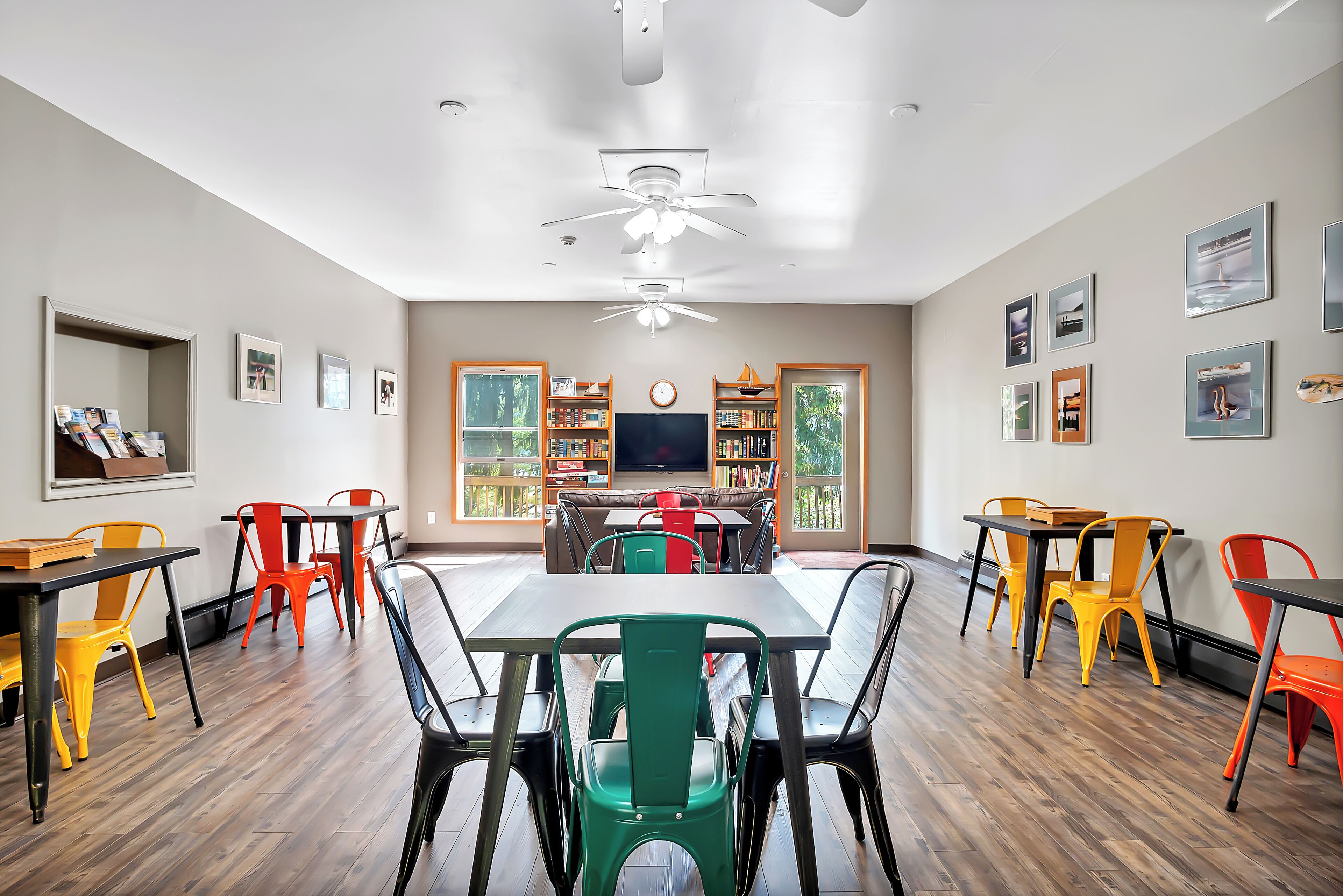 A dining area with tables and chairs, a ceiling fan, and a bookshelf with books and decorative items.
