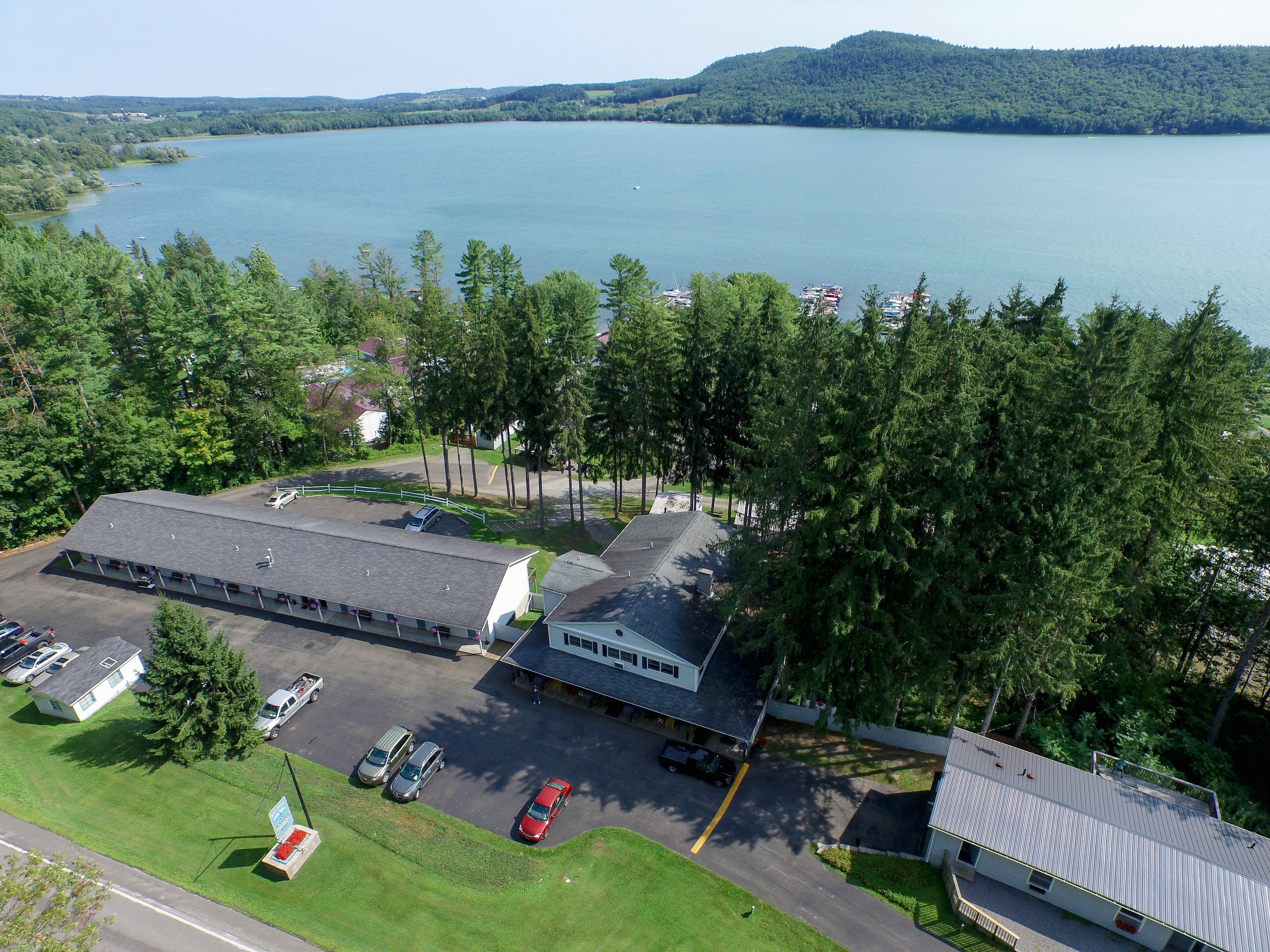An aerial view of a building with a parking lot, surrounded by trees and a lake.