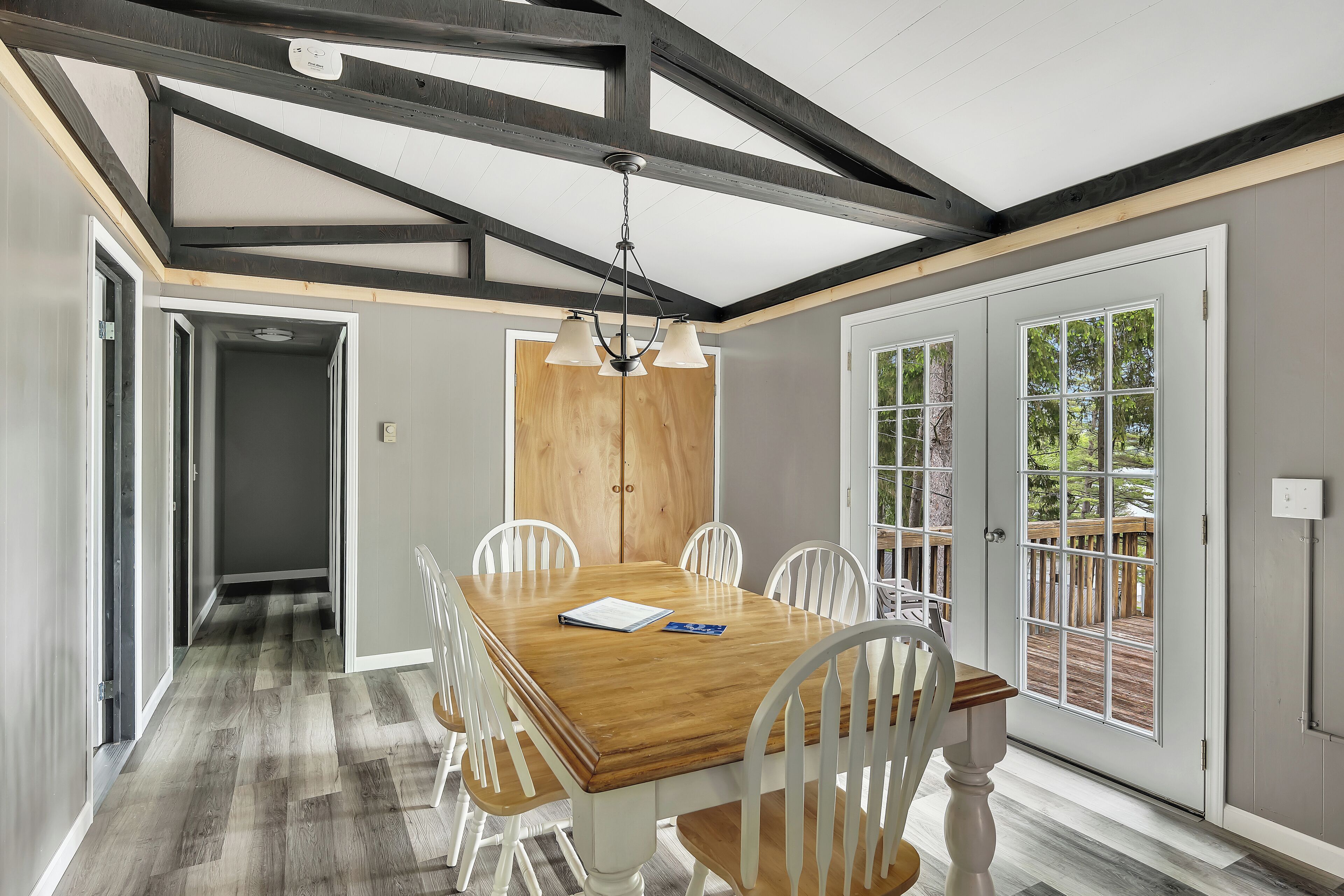A dining area with a wooden table and white chairs, a chandelier, and a view through a glass door.