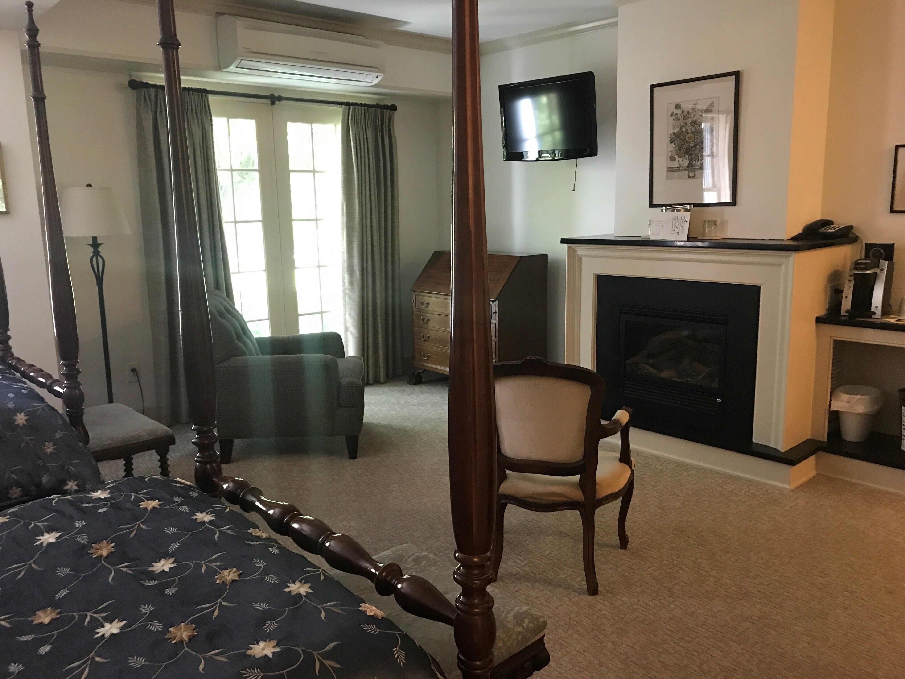 A four-poster bed, a television, a fireplace, and a chair in a room with a carpeted floor.